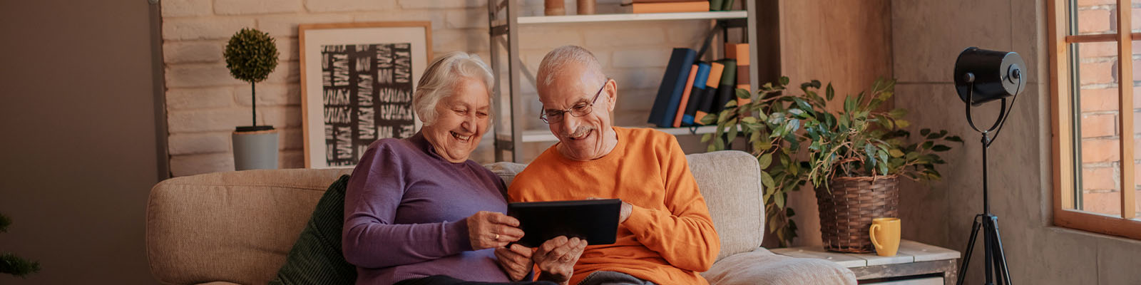 A senior man and woman sitting together on a couch looking down at a tablet
