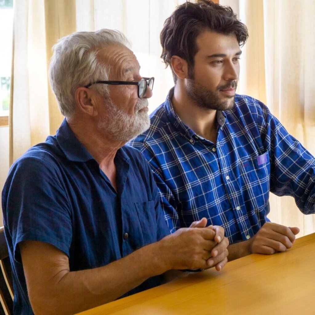 An image of a father and daughter sitting next to each other on a couch, smiling and laughing together.