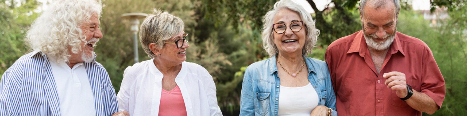 A group of 2 senior couples walking together outside and smiling.
