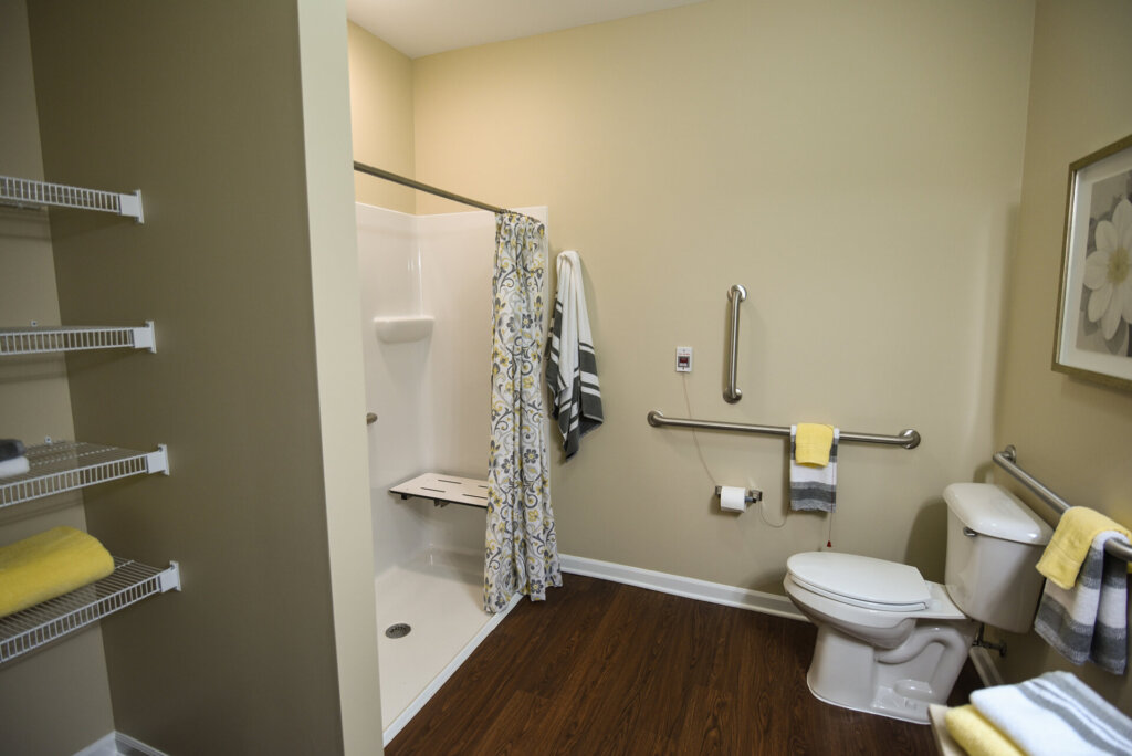 model bathroom of a senior living unit at Traditions of Beavercreek featuring a walkin in shower and several decorations