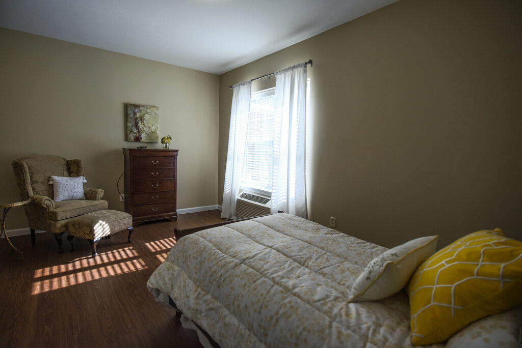 bedroom at Traditions of Beavercreek with a window letting in natural light, a dresser and a cushioned chair & ottoman